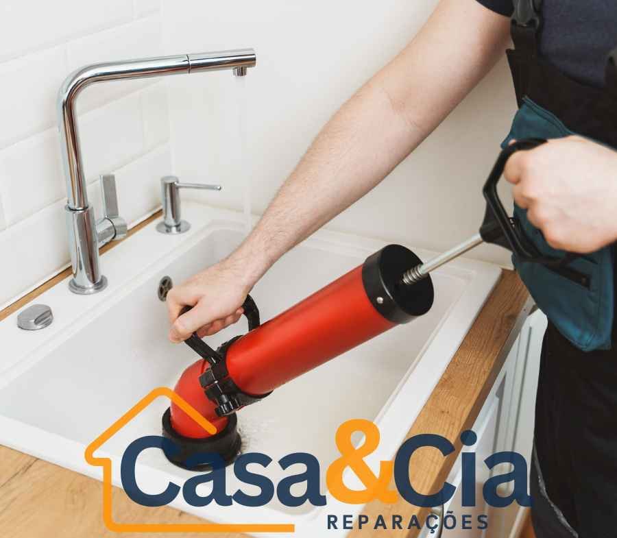 Desentupidor hidráulico sendo usado em pia de cozinha para remoção de obstruções no encanamento.